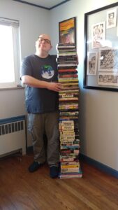 The author, next to a nose-high stack of one copy of everything he's published